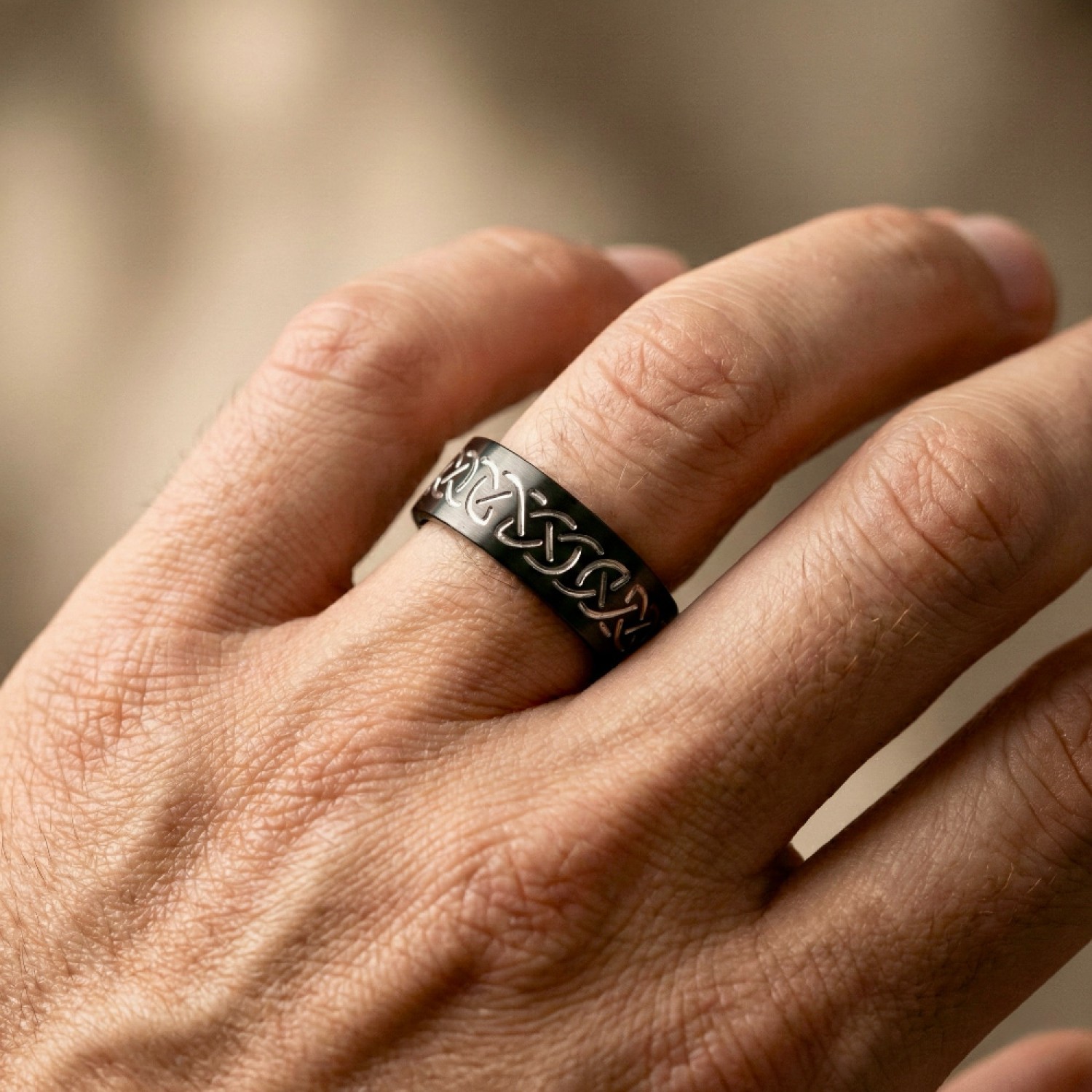 A polished black zirconium wedding ring featuring a contrasting engraved silver-toned Celtic eternity knot pattern, cast against a white background with a reflection below.