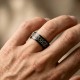 A polished black zirconium wedding ring featuring a contrasting engraved silver-toned Celtic eternity knot pattern, cast against a white background with a reflection below.
