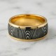 The Strata Wedding Ring: A polished yellow gold band featuring a central inlay of laser-carved black zirconium with a wavy woodgrain pattern, standing on a white background.